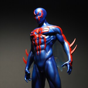 May include: A blue and red action figure of a superhero with a spider symbol on the chest. The figure has a detailed muscular build and a mask with a spider design.