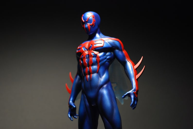 May include: A blue and red action figure of a superhero with a spider symbol on the chest. The figure has a detailed muscular build and a mask with a spider design.