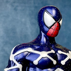 Puede incluir: Una figura de superh&eacute;roe azul y blanca con un dise&ntilde;o de ara&ntilde;a roja en la m&aacute;scara. La figura tiene un patr&oacute;n de cielo estrellado en el traje.