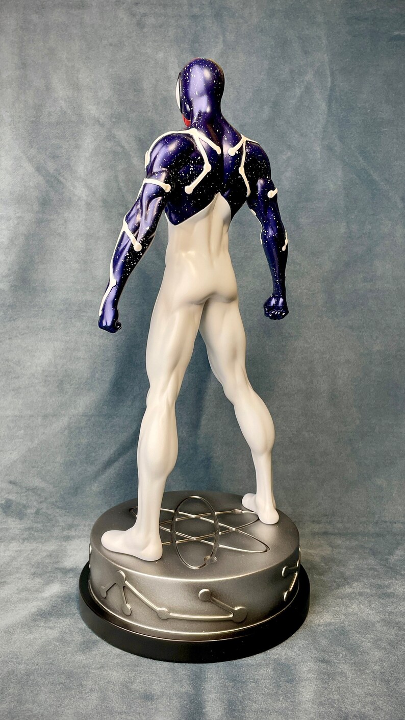 Puede incluir: Una figura de superh&eacute;roe blanca y azul con un patr&oacute;n estrellado. La figura est&aacute; de pie sobre una base plateada con un dise&ntilde;o circular.