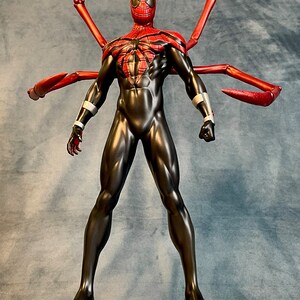 May include: A black and red action figure of Spider-Man with long red arms, standing on a silver base with a black rim. The figure has a red and black spider-web design on its chest.