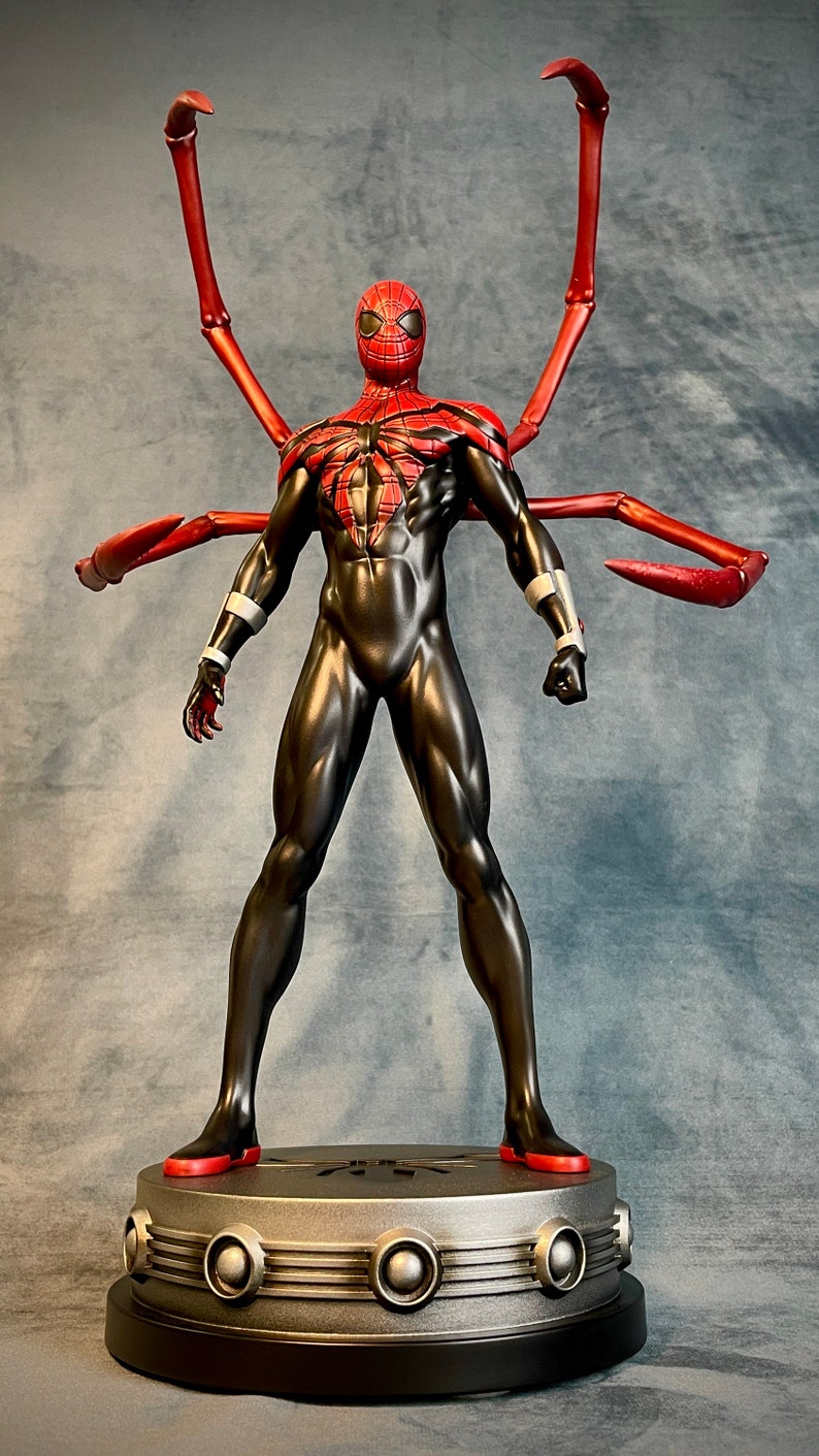 May include: A black and red action figure of Spider-Man with long red arms, standing on a silver base with a black rim. The figure has a red and black spider-web design on its chest.