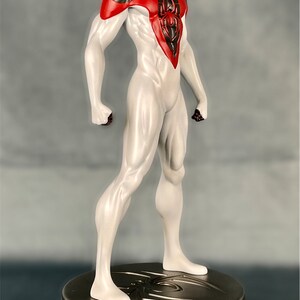 May include: A white and black action figure of Spider-Man with red accents. The figure is standing on a round, metallic base with a spider design.