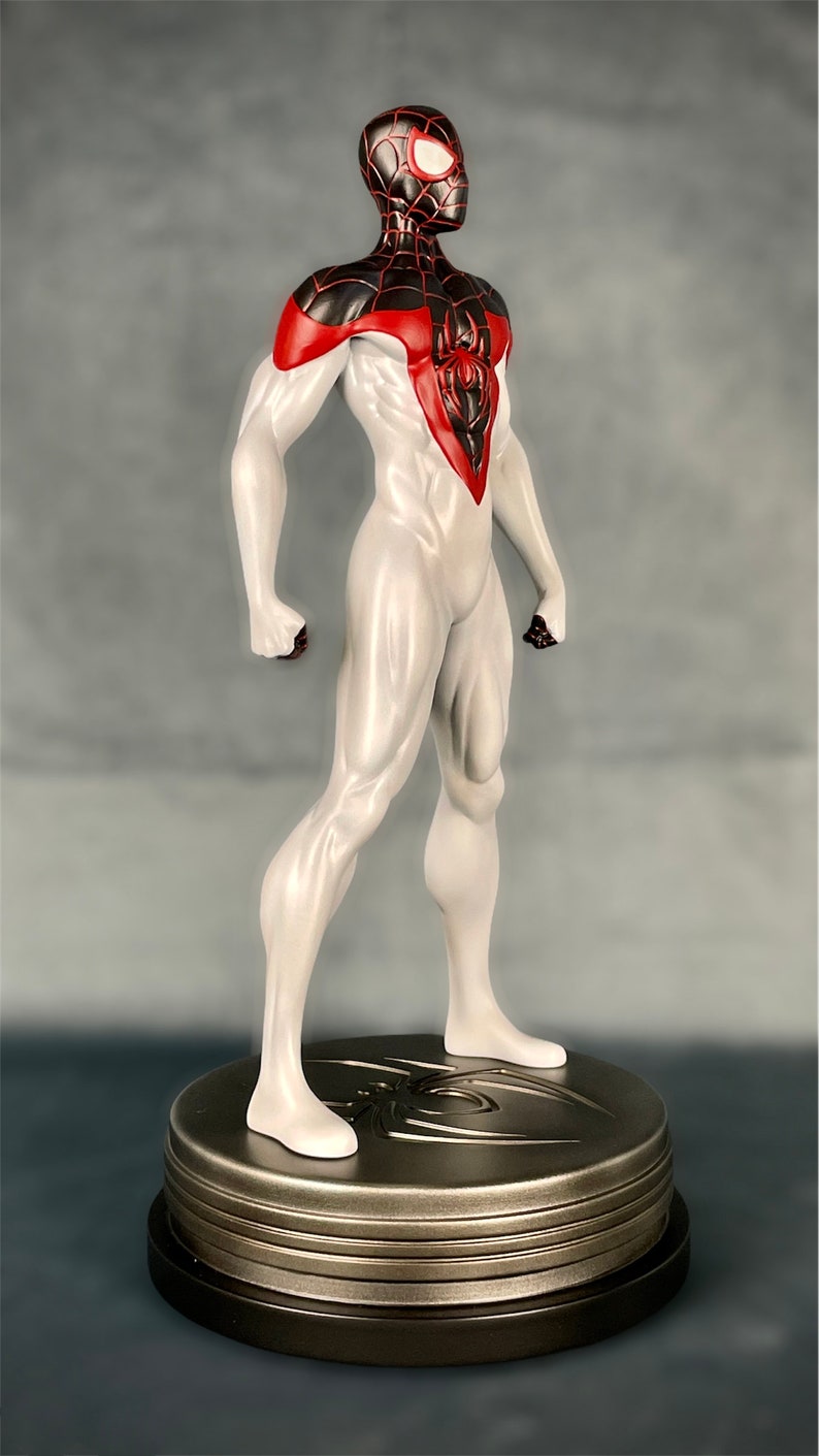 May include: A white and black action figure of Spider-Man with red accents. The figure is standing on a round, metallic base with a spider design.
