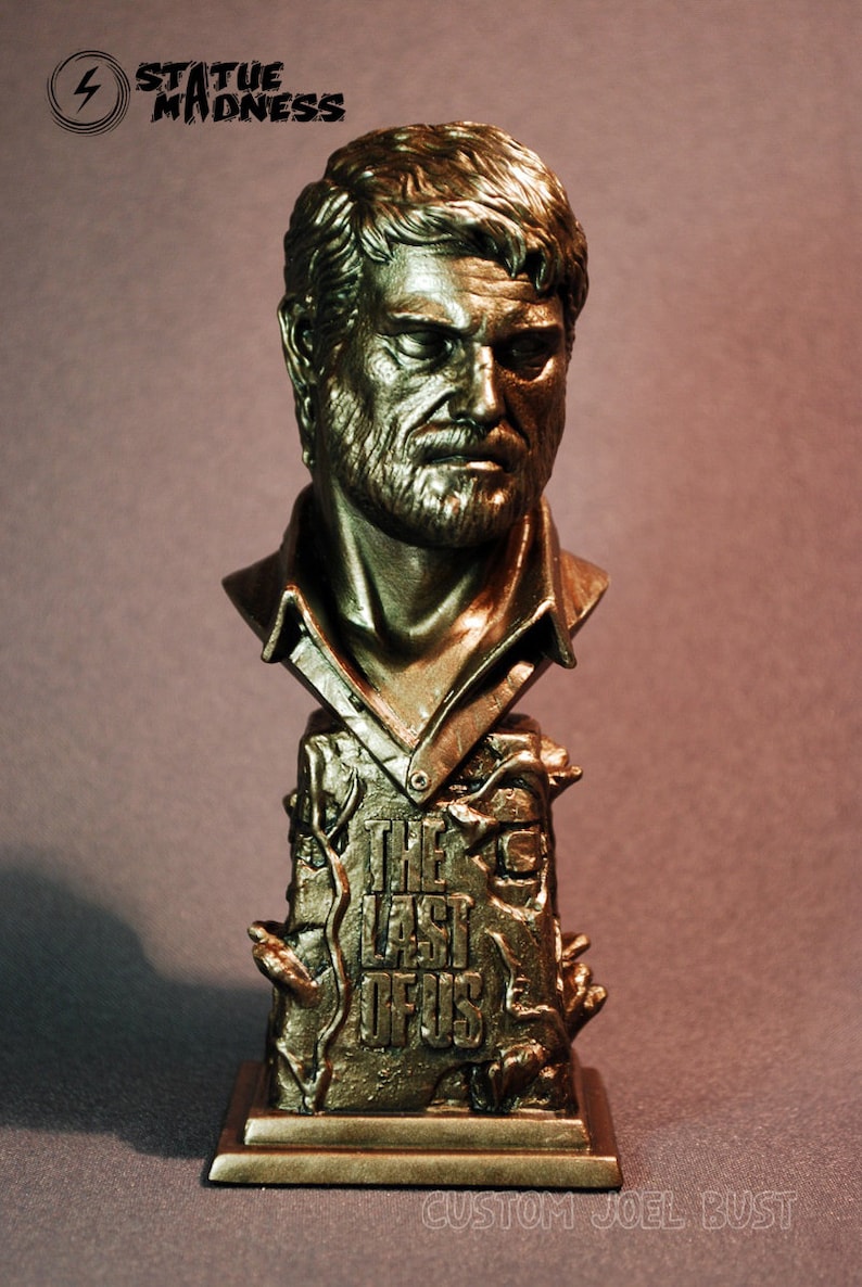 Pu&ograve; includere: Un busto dorato di Joel dal videogioco "The Last of Us". Il busto &egrave; su una base con il logo del gioco e le parole "Custom Joel Bust."
