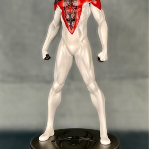 May include: A white and black action figure of Spider-Man with red accents. The figure is standing on a round, metallic base with a spider logo.