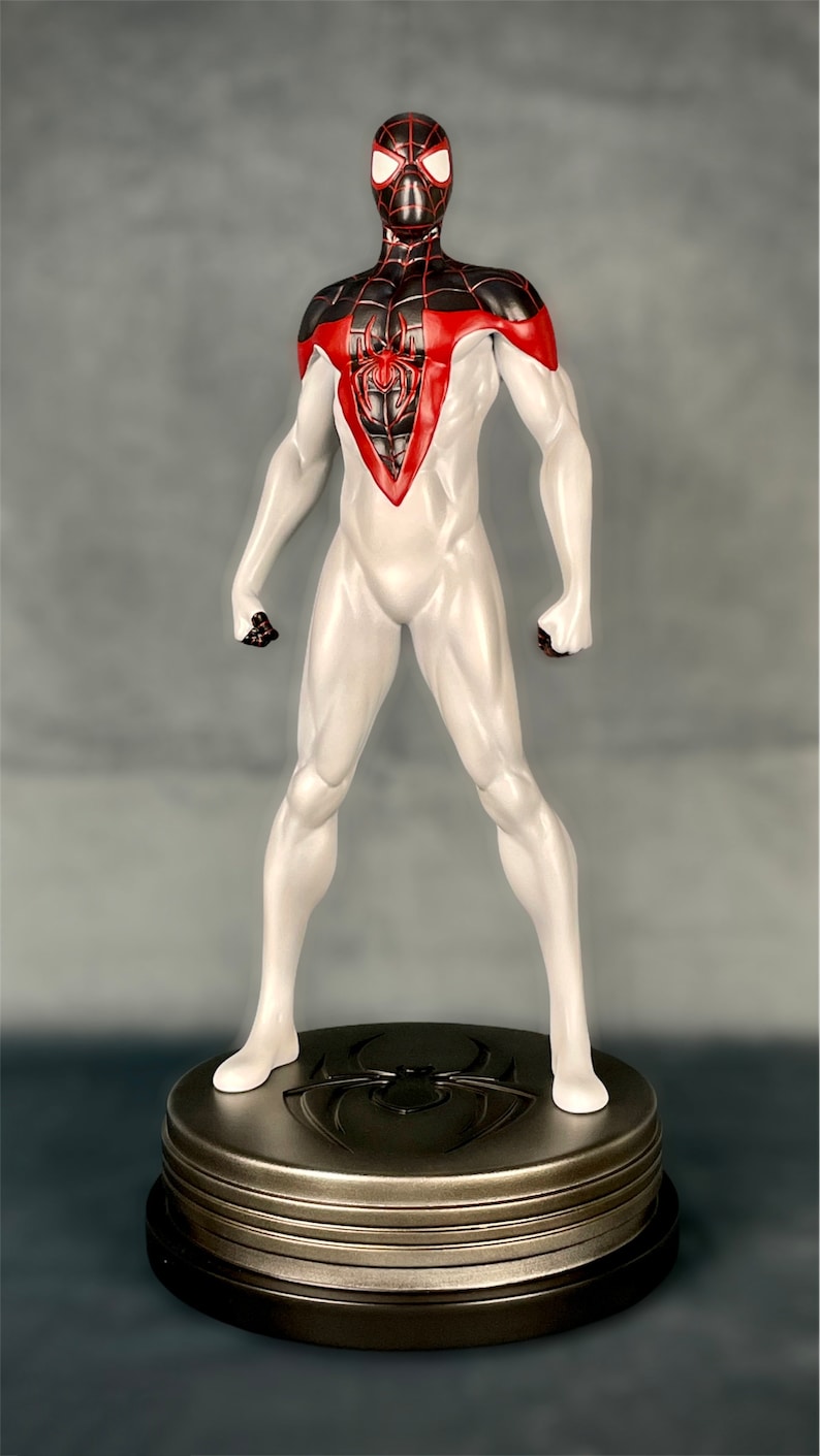 May include: A white and black action figure of Spider-Man with red accents. The figure is standing on a round, metallic base with a spider logo.