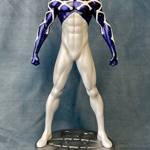 Puede incluir: Una figura de acci&oacute;n blanca y azul de un superh&eacute;roe con una m&aacute;scara roja y negra. La figura est&aacute; de pie sobre una base plateada con un s&iacute;mbolo de &aacute;tomo.