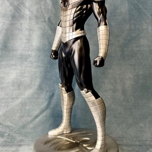 May include: A silver and black action figure of Spider-Man standing on a silver base with a spider web design. The figure is posed in a dynamic stance with one leg forward and arms raised.