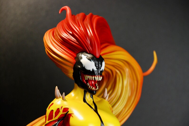 May include: A detailed figurine of a female character with a black and white face, red mouth, and spiky teeth. The figure has a yellow torso, red and yellow accents, and long, flowing hair in shades of red and yellow. The figure has sharp, spiky shoulder pads.