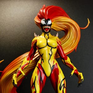 May include: A detailed figurine of a female character with a yellow and red bodysuit. The figure has long, flowing hair in shades of red and orange. The face is white with black markings and sharp teeth. The figure is posed with arms outstretched.