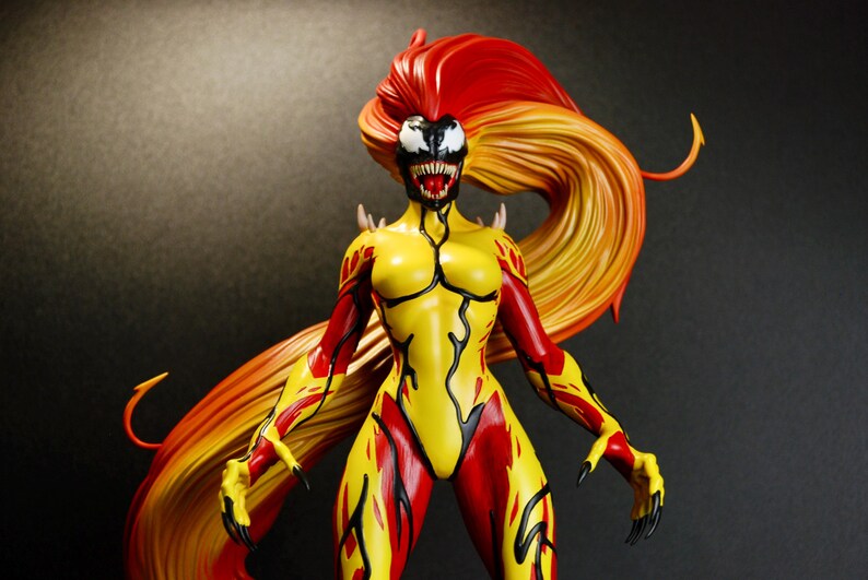 May include: A detailed figurine of a female character with a yellow and red bodysuit. The figure has long, flowing hair in shades of red and orange. The face is white with black markings and sharp teeth. The figure is posed with arms outstretched.