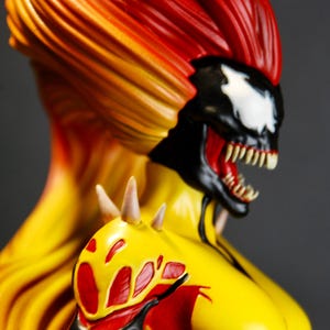 May include: A detailed bust of a comic book character with a fiery color scheme. The figure features a black and white face with sharp teeth, red mouth, and a yellow and red hair. The shoulder has a yellow and red design.