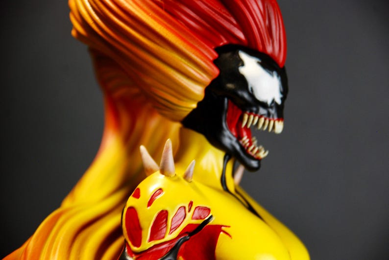 May include: A detailed bust of a comic book character with a fiery color scheme. The figure features a black and white face with sharp teeth, red mouth, and a yellow and red hair. The shoulder has a yellow and red design.