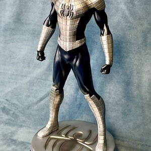 May include: A silver and black action figure of Spider-Man in a metallic suit. The figure is standing on a circular base with a spider logo.
