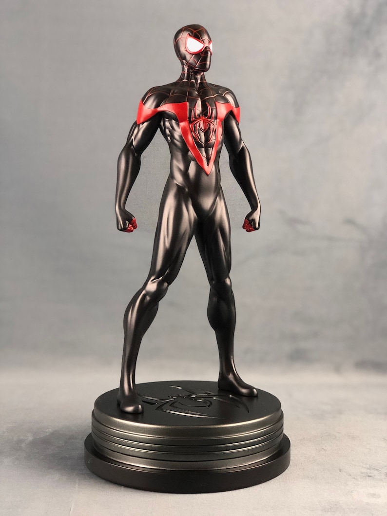 May include: Black and red Spider-Man action figure with a black base. The figure is posed in a heroic stance with its arms outstretched.