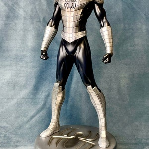 May include: A silver and black action figure of Spider-Man standing on a circular base with a spider logo. The figure is wearing a silver and black suit with a spider logo on the chest.