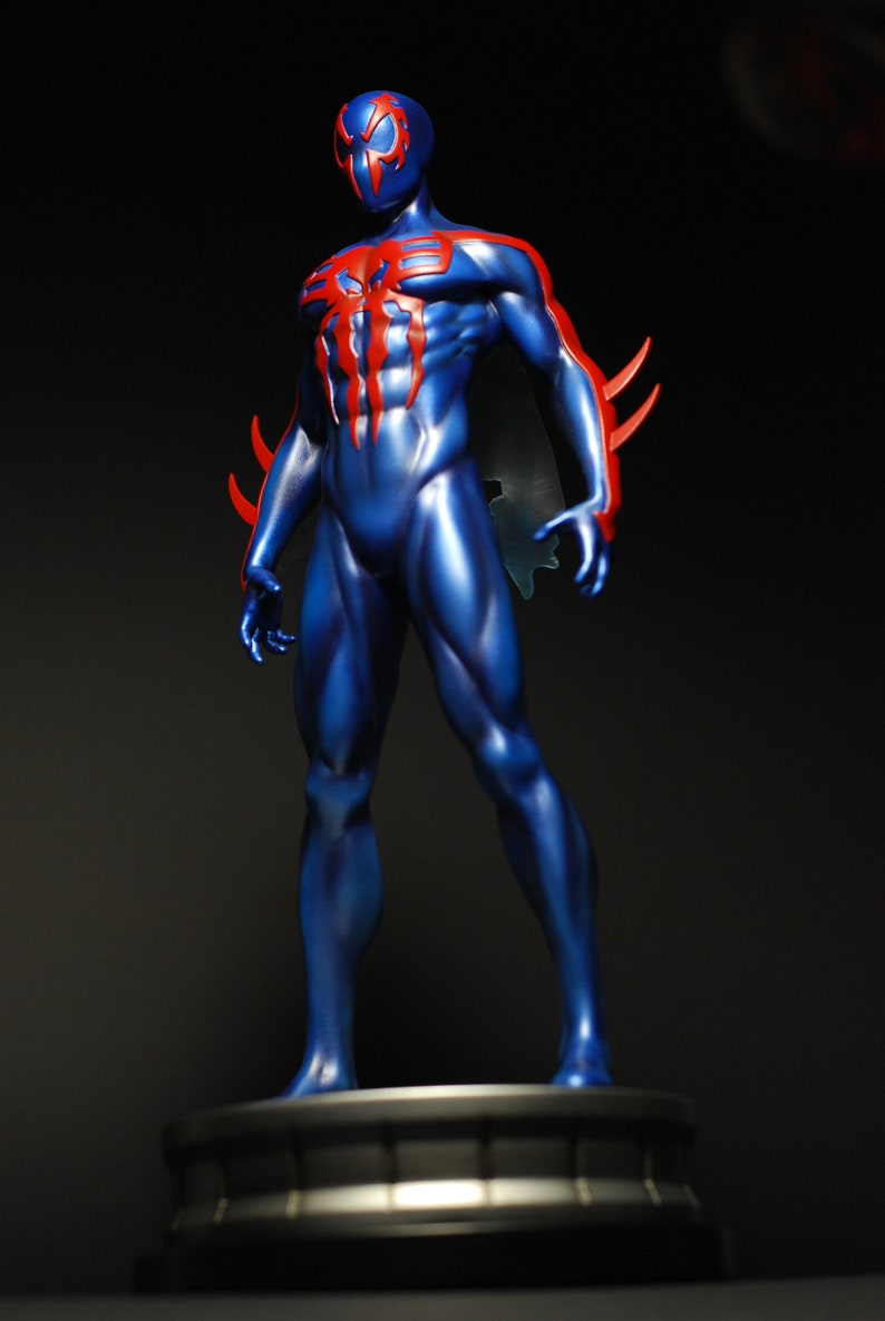 May include: A blue and red action figure of a superhero with a spider design on the chest. The figure is standing on a black base.