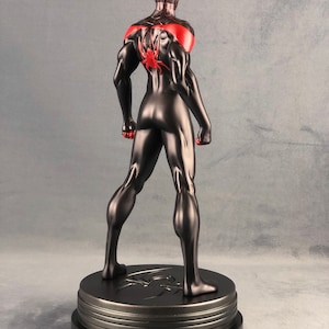 May include: Black and red action figure of Spider-Man standing on a black base. The figure is posed with its arms raised and fists clenched. The figure is wearing a black suit with red accents and a spider logo on the back.