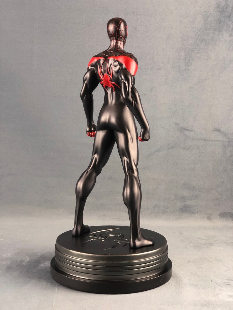 May include: Black and red action figure of Spider-Man standing on a black base. The figure is posed with its arms raised and fists clenched. The figure is wearing a black suit with red accents and a spider logo on the back.