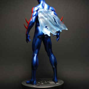 May include: A blue and red superhero action figure with a translucent cape standing on a black base.