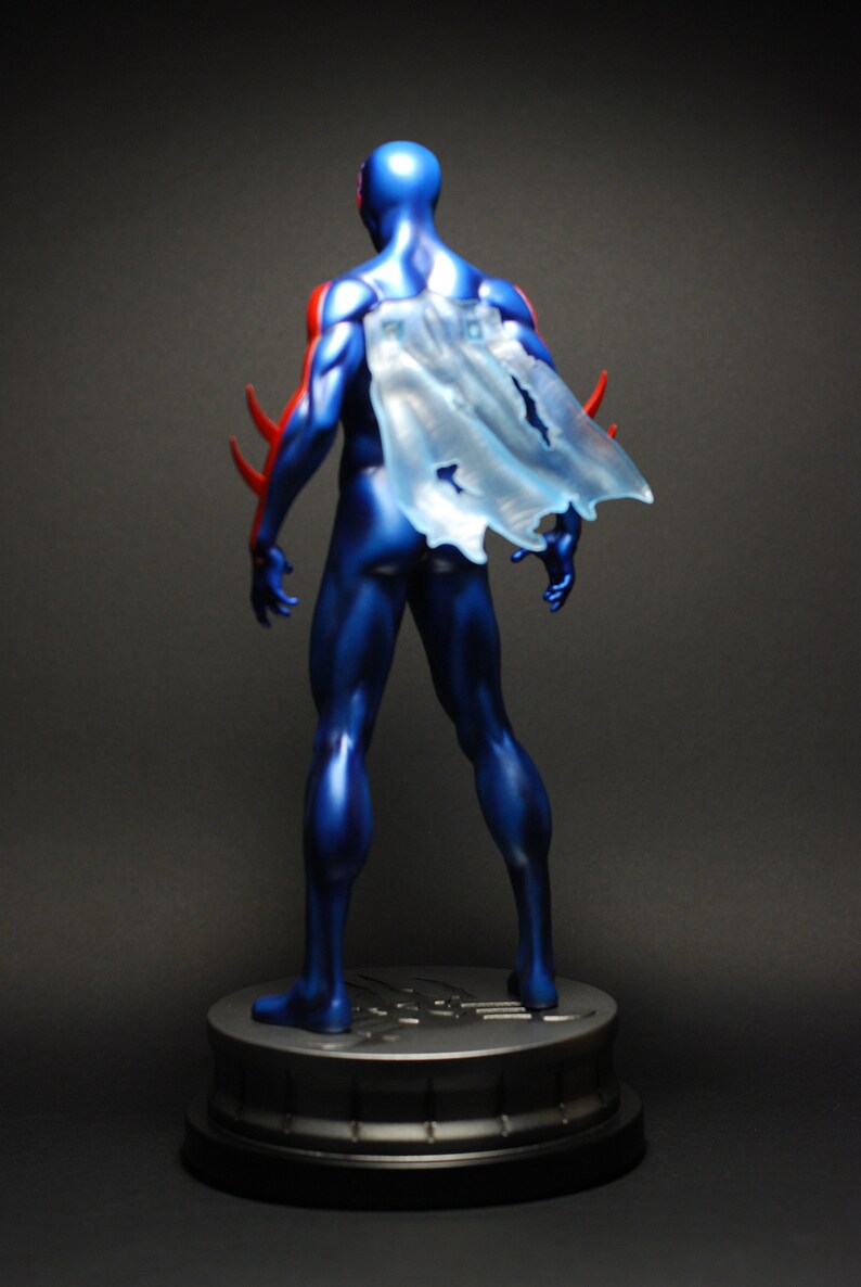 May include: A blue and red superhero action figure with a translucent cape standing on a black base.