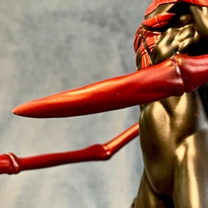 May include: A black and red action figure with long, red, articulated arms. The figure has a silver and red wrist band.