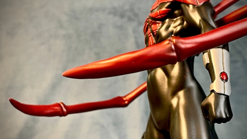 May include: A black and red action figure with long, red, articulated arms. The figure has a silver and red wrist band.