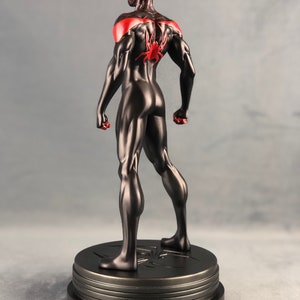 May include: Black and red superhero action figure standing on a black base with a spider symbol. The figure is posed with arms outstretched and legs slightly apart.