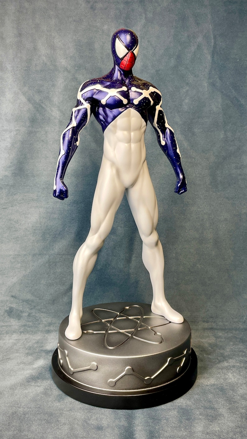 Puede incluir: Una figura de acci&oacute;n blanca y morada de un superh&eacute;roe que lleva una m&aacute;scara y un traje con un patr&oacute;n de estrellas. La figura est&aacute; de pie sobre una base plateada con un s&iacute;mbolo de &aacute;tomo.