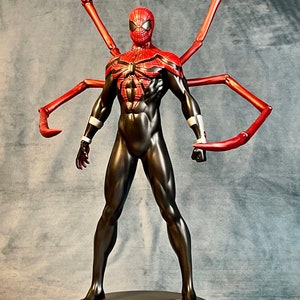 May include: A red and black action figure of Spider-Man with long red spindly arms. The figure is standing on a round base with a spider symbol in the center.