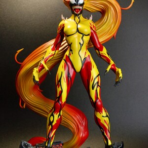 May include: A detailed figurine of a female character with a yellow and red color scheme. The figure has long, flowing hair in shades of red and yellow. The character is posed on a rocky base, with a menacing expression and clawed hands.