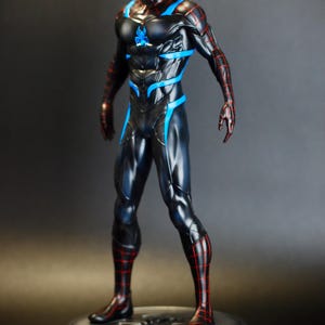May include: A black and blue superhero figurine with red accents, standing on a silver base. The figure has a detailed costume with a spiderweb pattern and blue highlights. The figurine is a collectible item.