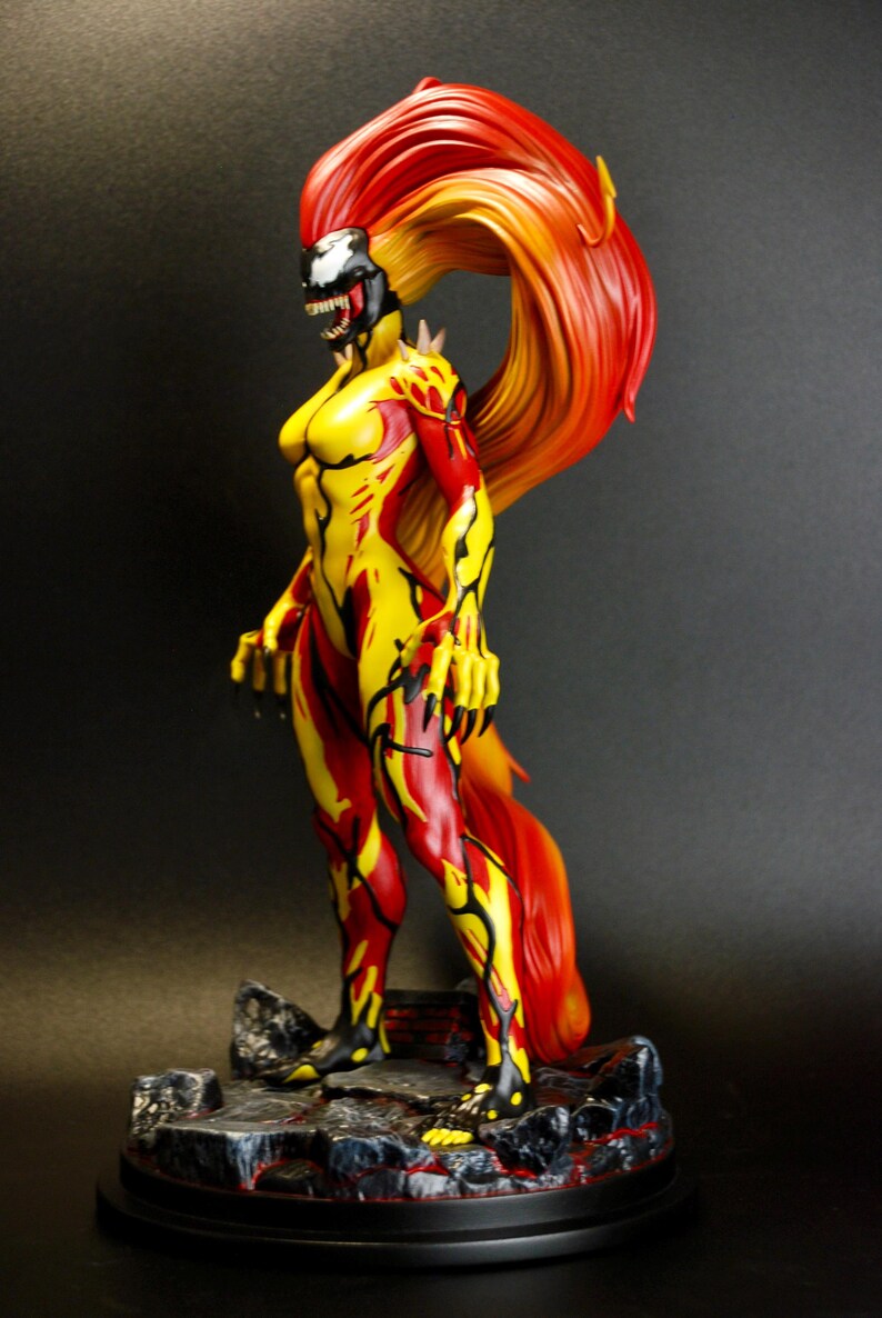 May include: A detailed figurine of a female character with a fiery red and yellow color scheme. The figure has a black and white face, and the hair flows dramatically. The character is posed on a rocky base, with a black background.