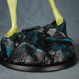 May include: A green-skinned figure stands on a rocky base with a black circular base. The base is painted with a dark blue and black color scheme.