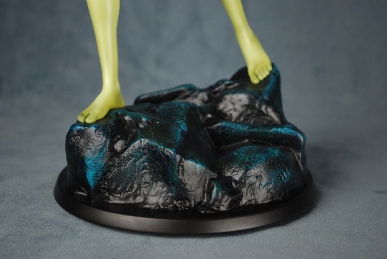 May include: A green-skinned figure stands on a rocky base with a black circular base. The base is painted with a dark blue and black color scheme.