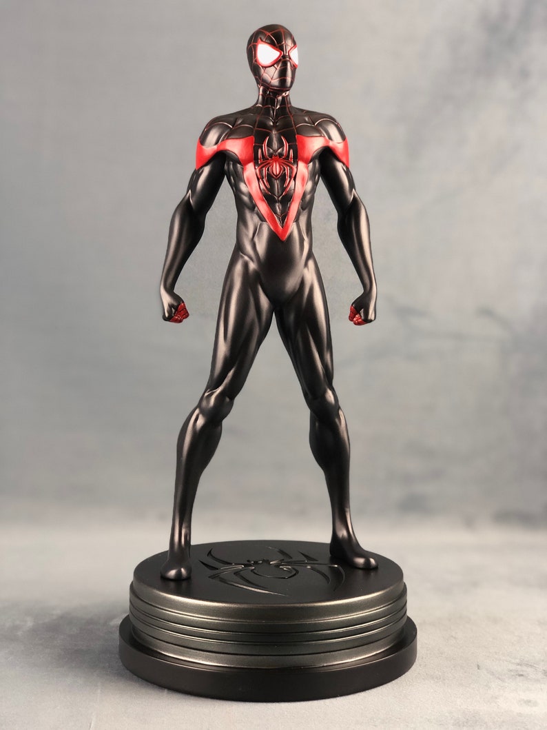 May include: Black and red Spider-Man action figure with a black base. The figure is standing with its arms outstretched and has a red spider symbol on its chest.