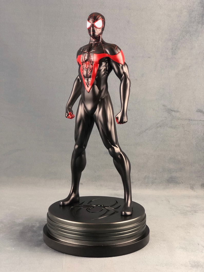 May include: Black and red Spider-Man action figure with a black base. The figure is posed with its arms out and its fists clenched. The figure is standing on a black base with a spider web design.