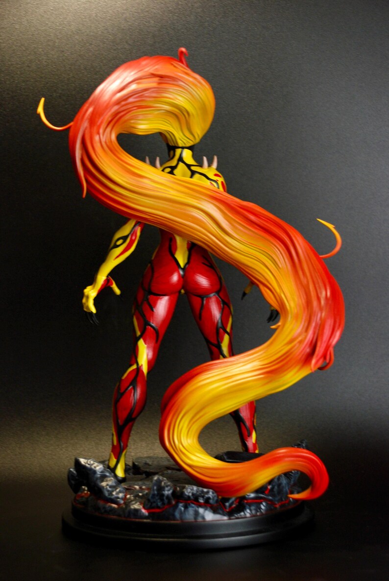 May include: A figurine of a female character with fiery red and yellow hair cascading down her back. The figure is in a dynamic pose, with red and yellow detailing on the body. The base is a dark, textured surface.