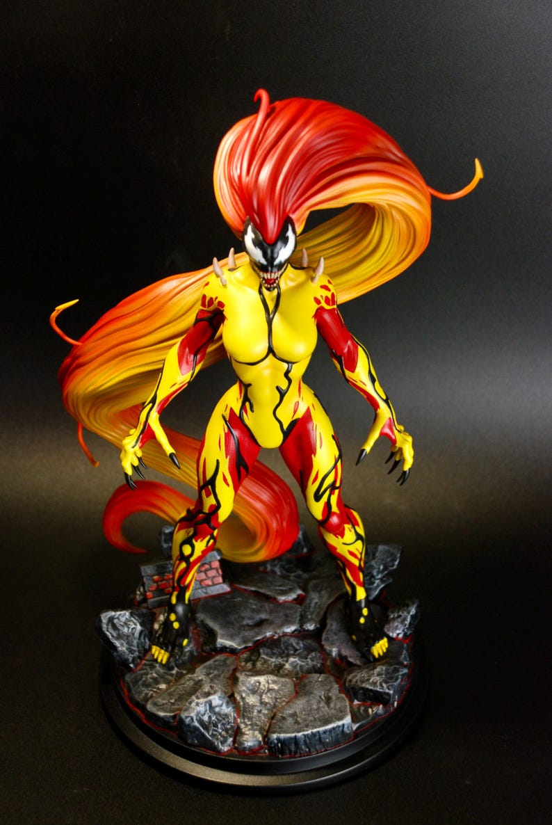 May include: A detailed figurine of a female superhero with a yellow and red color scheme. The figure has long, flowing orange and red hair. The base is a rocky terrain with a black circular base. The figure is in a dynamic pose, with sharp claws and a menacing expression.