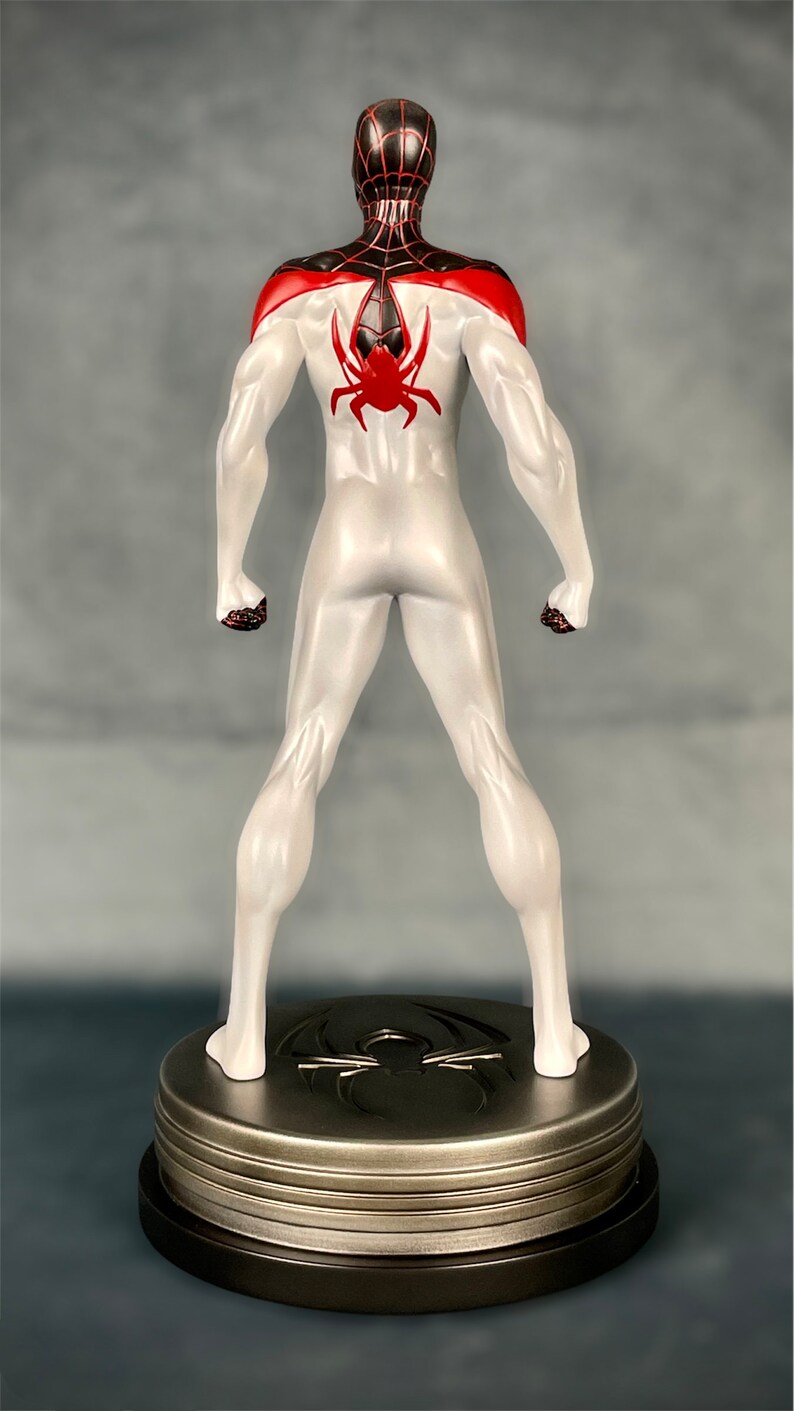 May include: A white and red action figure of Spider-Man standing on a black and silver base. The figure is posed with its arms at its sides and its legs slightly apart. The figure has a black spider symbol on its back.