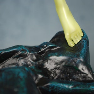 May include: A green foot sculpture stepping on a black and teal rock sculpture.