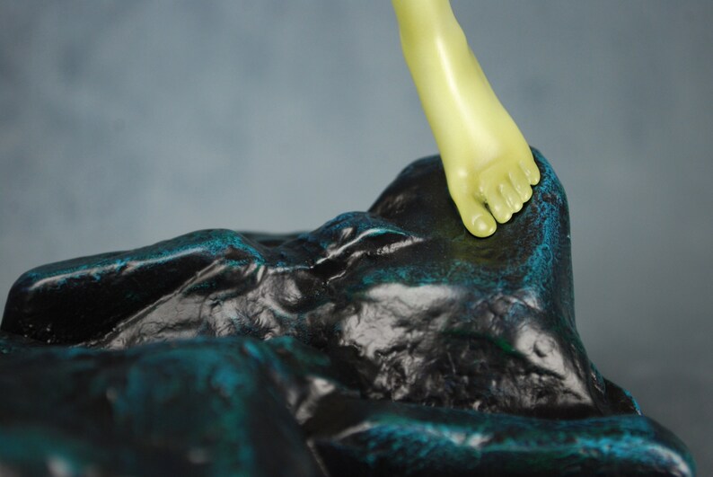 May include: A green foot sculpture stepping on a black and teal rock sculpture.