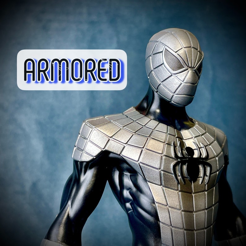 May include: A silver and black armored Spider-Man action figure with a black spider logo on the chest. The figure is posed with its arms raised and its head tilted slightly to the side. The word "ARMORED" is written in blue letters on a white background in the top left corner of the image.