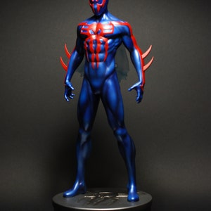 May include: A blue and red action figure of Spider-Man in a dynamic pose, standing on a black base. The figure has a detailed sculpt and paint job, with a red spider symbol on the chest.