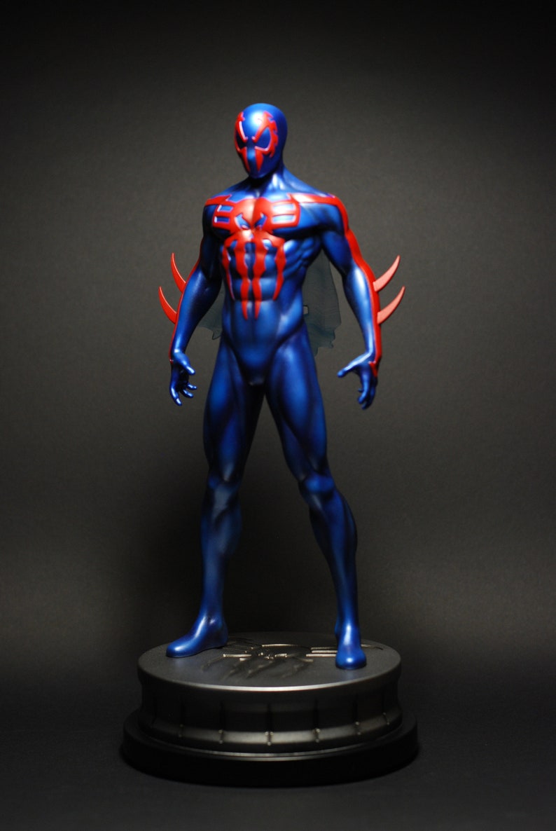 May include: A blue and red action figure of Spider-Man in a dynamic pose, standing on a black base. The figure has a detailed sculpt and paint job, with a red spider symbol on the chest.
