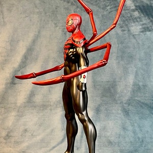 May include: A red and black action figure of Spider-Man with long, red, articulated arms. The figure is standing on a silver base with a black rim.