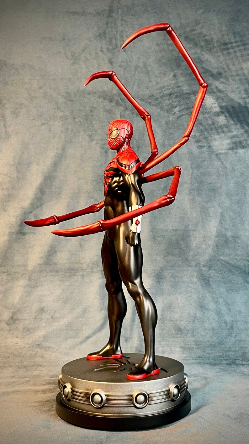 May include: A red and black action figure of Spider-Man with long, red, articulated arms. The figure is standing on a silver base with a black rim.