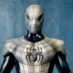 May include: A silver and black Spider-Man costume with a textured, metallic finish. The costume features a black spider logo on the chest.