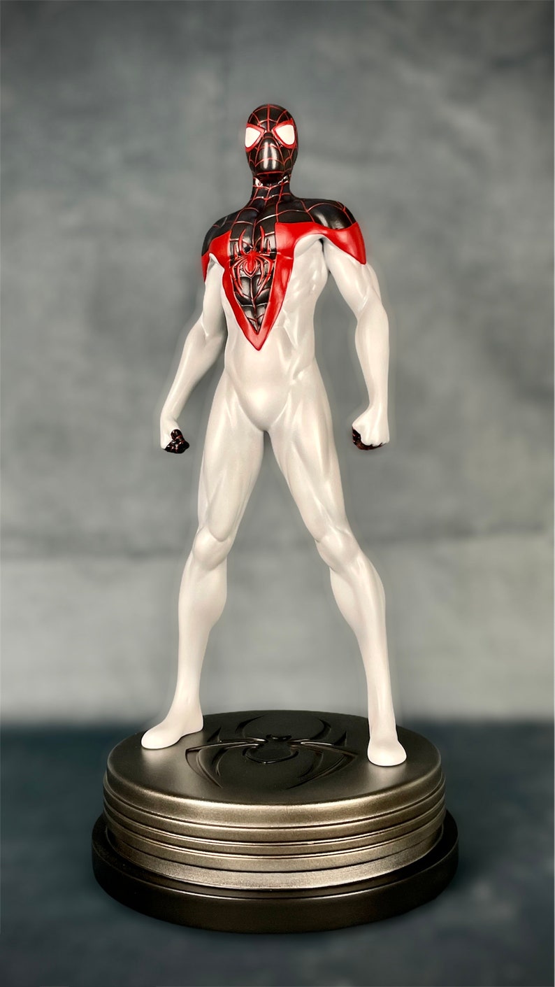 May include: A white and black Spider-Man action figure with red accents stands on a metallic base with a spider logo. The figure is posed in a heroic stance with arms outstretched.